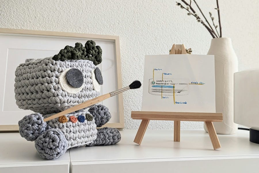 Knitted robot pointing paint brush at an easel with words on it
